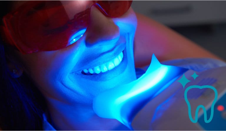 A woman undergoing a teeth whitening procedure, illuminated by blue light, showcasing her brightening smile.
